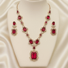 Rose gold necklace set with ruby-red oval and emerald-cut stones, diamond-inspired detailing, and matching earrings, displayed on a satin background, showcasing luxurious bridal jewellery design.