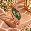 Rose gold premium brass cuff bracelet featuring emerald green zirconia stones, intricate scrollwork and sparkling clear stone accents.