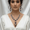 Rose gold necklace set with deep blue rectangular stones and an ornate central pendant, paired with matching drop earrings, displayed on a cream jewellery stand against a satin backdrop.