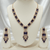 Rose gold necklace set with deep blue rectangular stones and an ornate central pendant, paired with matching drop earrings, displayed on a cream jewellery stand against a satin backdrop.