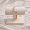Rose gold bracelet with a heart-shaped clasp on a beige stand against a soft pink background