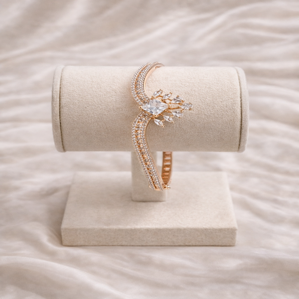 Rose gold bracelet with a heart-shaped clasp on a beige stand against a soft pink background