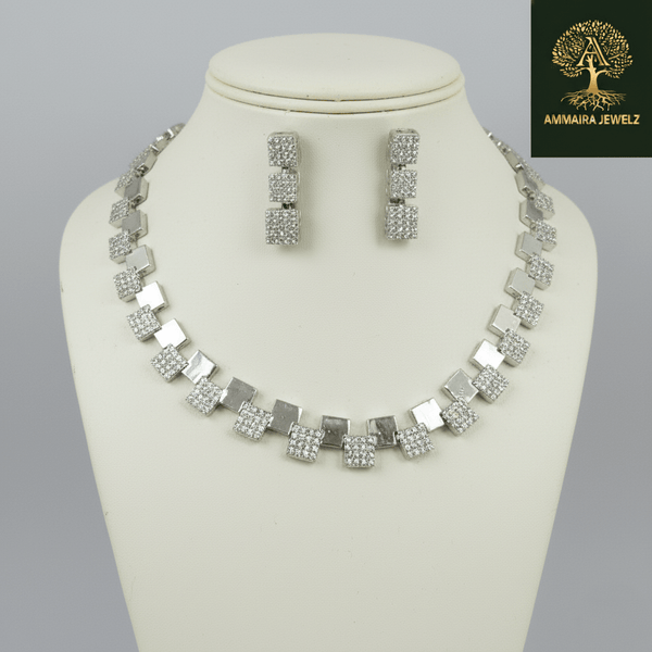 Silver necklace set with alternating square geometric motifs and matching drop earrings, displayed on a satin fabric background, showcasing modern minimal luxury jewellery design.