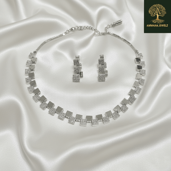Silver necklace set with alternating square geometric motifs and matching drop earrings, displayed on a satin fabric background, showcasing modern minimal luxury jewellery design.