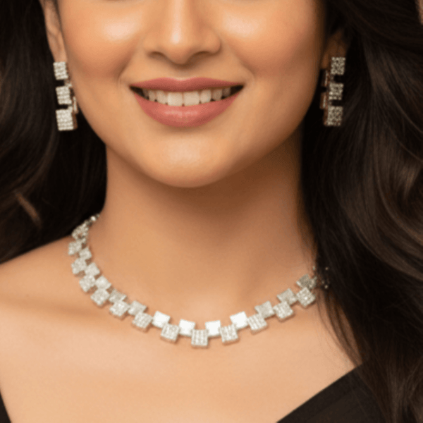 Silver necklace set with alternating square geometric motifs and matching drop earrings, displayed on a satin fabric background, showcasing modern minimal luxury jewellery design.