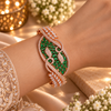 Rose gold premium brass cuff bracelet featuring emerald green zirconia stones, intricate scrollwork and sparkling clear stone accents.