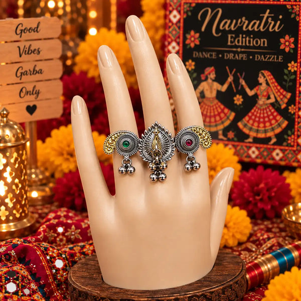 Two-tone fusion oxidised three-finger statement ring featuring a central peacock, golden paisley accents, green and red stones, and dangling ghungroos.
