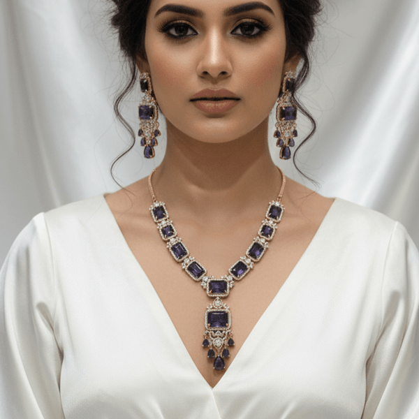 Rose gold necklace set with deep blue rectangular stones and an ornate central pendant, paired with matching drop earrings, displayed on a cream jewellery stand against a satin backdrop.